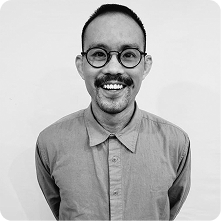 A smiling man with a mustache wearing round glasses and a button-up shirt, standing against a plain white background. This image is intended for the 'About Us' page.