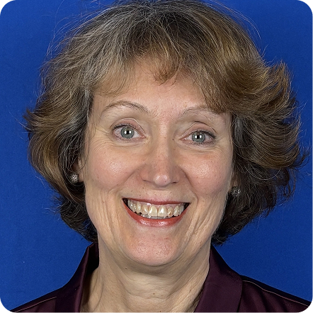 A woman with short, layered brown hair, wearing a dark maroon blouse, smiling against a blue background. Her posture is upright, and she appears to be looking directly at the camera.